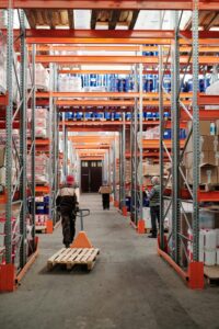 Workers arrange inventory on shelves in a large industrial warehouse.